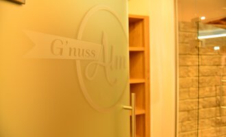 Eine Tür mit dem Schriftzug „G'nuss Alm“ ist im Bild sichtbar. Der Bereich scheint einladend und modern gestaltet zu sein. | © Hotel Alpenstüble Appartements | Manuel Riezler