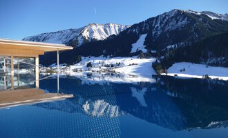 Ein Infinity-Pool mit Blick auf schneebedeckte Berge. Der klare Himmel und die ruhige Wasseroberfläche reflektieren die winterliche Landschaft. | © Hotel Erlebach | Kristin Winter