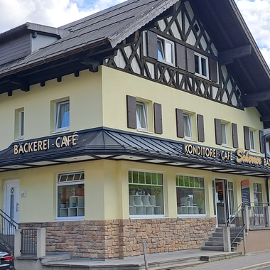 A nice café with a bakery in a traditional building. In the background, mountains and a blue sky are visible. | © Kleinwalsertal Tourismus | Steffen Stöhr