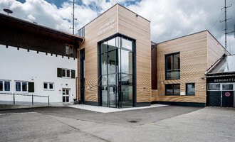 Ein modernes Gebäude mit Holzfassade und großen Glasfenstern. Es befindet sich in einer ländlichen Umgebung mit anderen traditionellen Gebäuden. | © Feuerwehr Riezlern | Gemeinde Mittelberg