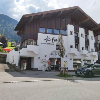 Ein modernes Gebäude mit Holz- und Putzfassade, das Apartments anbietet. Im Hintergrund sind grüne Berge und ein blauer Himmel zu sehen. | © Kleinwalsertal Tourismus | N. Lughammer