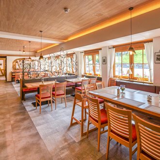 A modern restaurant with wooden furniture and an inviting atmosphere. Large windows let in plenty of daylight and offer a view of the outside. | © Familienhotel Kleinwalsertal Hotelgesellschaft mbH