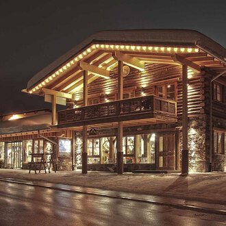 A cozy wooden building with warm light at night. The snow-covered ground and stylish design create an inviting atmosphere. | © Fun-Alp
