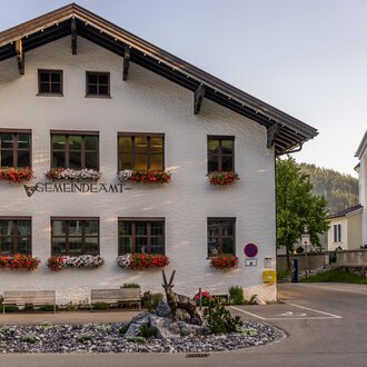 Ein charmantes Gemeindegebäude mit blühenden Blumenkästen. Im Hintergrund sind weitere Gebäude und Bäume zu sehen. | © Kleinwalsertal Tourismus |  Steffen Berschin