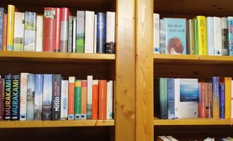 Ein Bücherregal mit einer Vielzahl von Buchrücken in verschiedenen Farben. Die Bücher sind ordentlich angeordnet und reichen von oben bis unten. | © Kleinwalsertal Tourismus | N. Lughammer