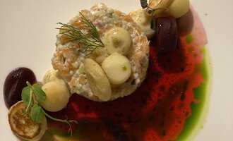 A beautifully arranged plate with a fish specialty, surrounded by various sauces and vegetables. The colors are vibrant and create an appealing visual impression.