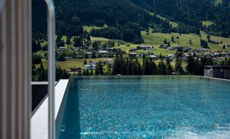 An infinity pool with sparkling water and a view of green hills. The surrounding landscape is mountainous and peaceful.