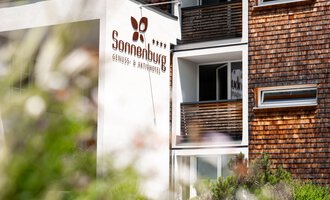 A modern building with the inscription "Sonnenburg". Surrounded by green vegetation and blooming plants.