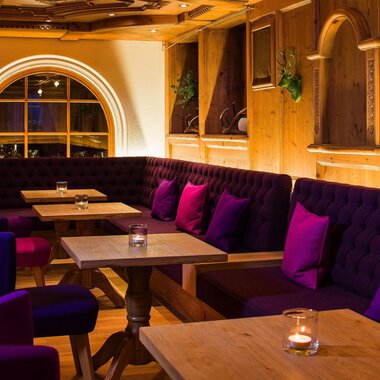 An inviting restaurant with cozy seating areas and warm wood interiors. The purple cushions on the benches create a relaxed atmosphere. | © Haller's Geniesserhotel | Dietmar Walser