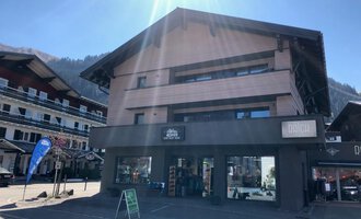 Ein modernes Gebäude mit mehreren Stockwerken, das eine Geschäftsfassade hat. Es befindet sich in einer malerischen Alpendorf-Umgebung. | © Sport Hilbrand OG