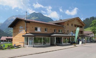 A modern wooden building in a picturesque mountain landscape. The clear skies and surrounding mountains give the place an inviting character. | © Sport Hilbrand OG