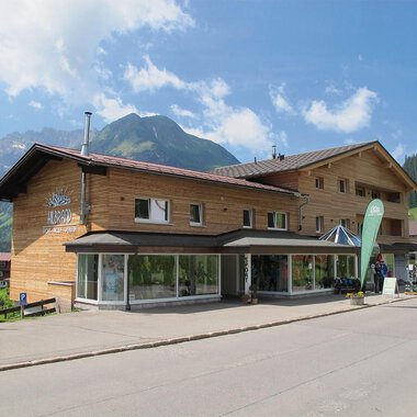 A modern wooden building in a picturesque mountain landscape. The clear skies and surrounding mountains give the place an inviting character. | © Sport Hilbrand OG