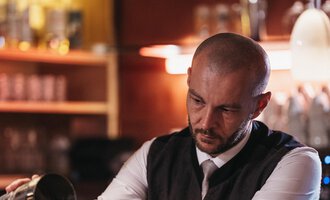 A bartender pours a drink into a glass. In the background, glasses and a stylish bar can be seen. | © Naturhotel Chesa Valisa | Heldentheater