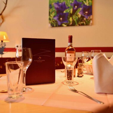 A beautifully set table in an elegant restaurant. On the table are glasses, a wine bottle, and a menu. | © IFA Breitach Apartements