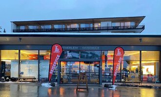 A modern ski and sports shop with large windows. Red flags with the inscription "Ski Center" stand in front of the entrance. | © Ifensport | Thomas MARTIN