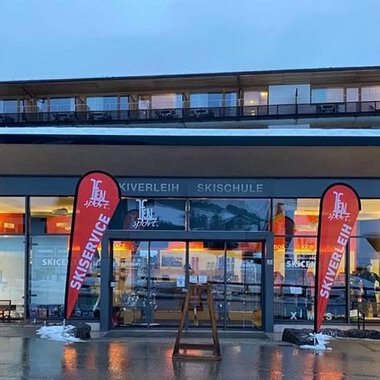 A modern ski and sports shop with large windows. Red flags with the inscription "Ski Center" stand in front of the entrance. | © Ifensport | Thomas MARTIN