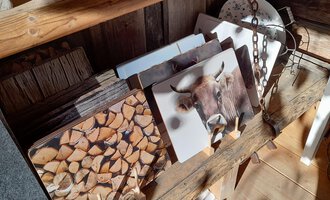A wooden bench with several pictures showing wooden logs and a cattle. The surroundings appear rustic and cozy. | © iKuh Schöne Ideen | Daniela Neumann