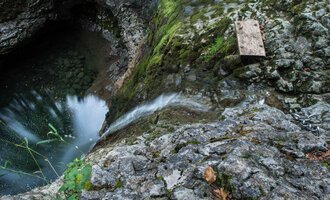 A rocky cliff with flowing water that leads into a deep, dark pool. Green moss and plants grow between the stones. | © Kleinwalsertal Tourismus | Andre Tappe