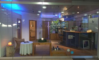 An inviting reception area with a bright, modern design. On the table, there is a candle and there are various products on the counter. | © Schönzeit | Sebastian Riezler