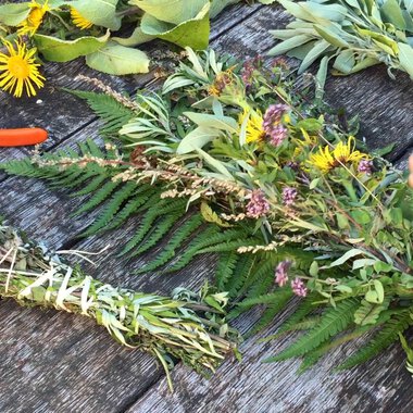 A table with fresh herbs and colorful flowers. Someone is tying a herb wreath with scissors beside it. | © Kleinwalsertal Tourismus | Lydia Fritz-Ilg