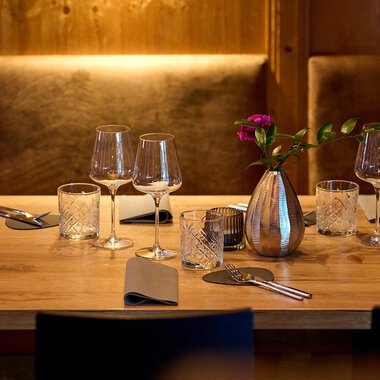 A beautifully set table in a cozy restaurant. It is decorated with glasses, cutlery, and a vase of flowers. | © La Vallée | Annette Sandner