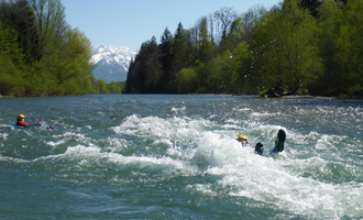 A river with foaming water and green trees along the shore. In the background, snow-capped mountains can be seen. | © MAP-Erlebnis