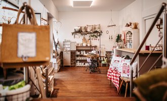 An inviting store with wooden flooring and stylish decorations.  
Shelves are filled with various products and cozy accessories.