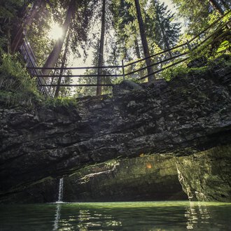 An idyllic place with clear waters and steep cliffs. In the background, tall trees and a sunbeam are visible. | © Kleinwalsertal Tourismus | Oliver Farys