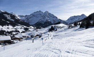 Eine verschneite Landschaft mit Bergen im Hintergrund. Skifahrer genießen die Pisten in dieser ruhigen Winterszene. | © OBERSTDORF · KLEINWALSERTAL BERGBAHNEN