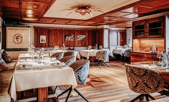 An elegant restaurant Sonnenstüble with wooden paneling and stylish chairs. Tables are set with white tablecloths and dishware, the atmosphere is cozy and inviting.