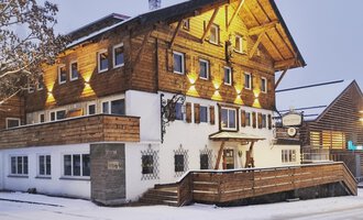 Ein charmantes Holzhaus im Schnee, beleuchtet von warmem Licht. Die Umgebung ist winterlich und einladend. | © Hotel Neue Krone GmbH | Werbewind GmbH