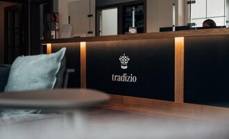 Ein moderner Empfangsbereich mit einem eleganten Empfangstresen. Das Logo "tradizio" ist gut sichtbar und wirkt einladend.