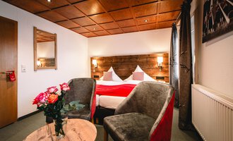 Ein gemütliches Schlafzimmer mit einem Doppelbett und modernen Möbeln. Zwei Sessel und ein Tisch ergänzen die warme Atmosphäre.