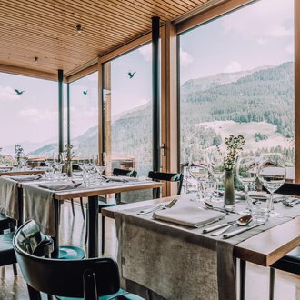A modern restaurant with large windows and a view of the mountains. The tables are elegantly set, creating an inviting atmosphere. | © Naturhotel Chesa Valisa | Heldentheater