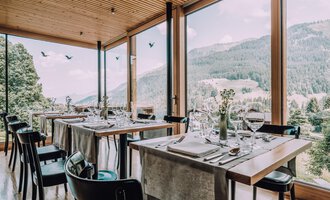A modern restaurant with large windows and a view of the mountains. The tables are elegantly set, creating an inviting atmosphere. | © Naturhotel Chesa Valisa | Heldentheater