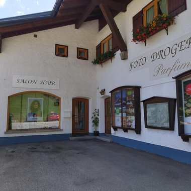 A charming building with blooming window boxes. It houses a salon and a drugstore. | © Kleinwalsertal Tourismus