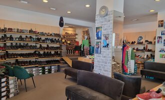 A shoe store with numerous shelves full of shoes. In the center, there are comfortable sofas, and clothing is on display. | © Schuhhaus Schuster | Marietta Diehl