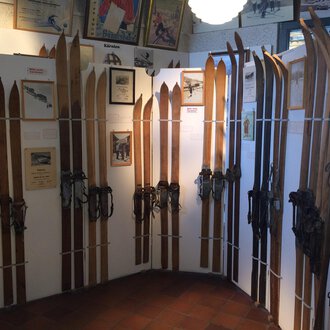 An exhibition featuring several wooden skis displayed on walls. In the background, photos and information about ski history are visible. | © Kleinwalsertal Tourismus | Blair Stevenson