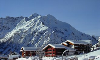 A picturesque mountain village in the snow with traditional wooden houses. In the background, majestic snow-capped peaks rise. | © IFA Hotel Alpenrose