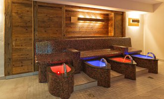 An elegant wellness area with four foot baths and a cozy seating bench. The soft lighting creates a relaxed atmosphere. | © Aparthotel Kleinwalsertal Haller GmbH & Co KG