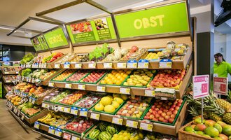 A colorful fruit shelf in a supermarket with fresh fruits like apples, bananas, and grapes. The shelves are well-filled and neatly arranged. | © SPAR