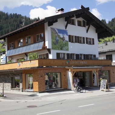 A charming building with traditional architecture, surrounded by mountains. On the ground floor, there is a shop with large windows. | © Sport Pauli Matthias Bischof e.U