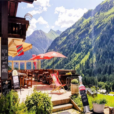 A cozy restaurant with terrace seating in the mountains. In the background, green forests and majestic mountains can be seen. | © Starzelhaus Pizzeria La Marmotta | J. Reich-Ulicny