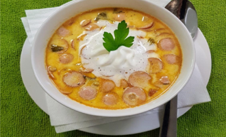 A creamy soup with slices of sausage and a dollop of cream. The soup is served in a white bowl on a white plate.
