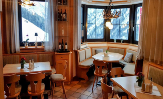 A cozy restaurant with wooden interiors and a view of the mountains. A round table and chairs invite you to linger.