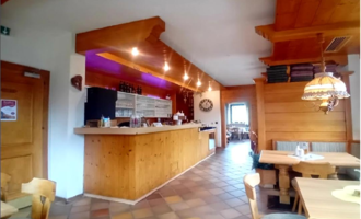 An inviting restaurant with a wooden counter area and warm lighting. The decor is cozy and rustic with wooden tables and chairs.