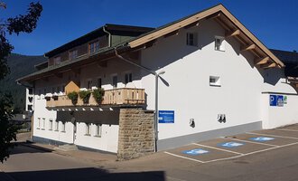 A modern building with a balcony and a parking space. The facade is bright and friendly, surrounded by mountains. | © Kleinwalsertal Tourismus