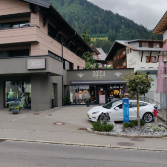 A modern shop in the mountains with a stylish facade. In front of the store, there is a white car and colorful flags are visible.