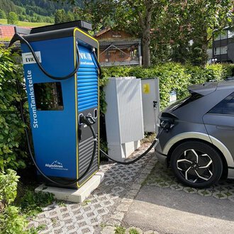 An electric charging station with an electric car that is currently being charged. The surroundings are green and peaceful, surrounded by trees. | © Energieversorgung Kleinwalsertal GmbH