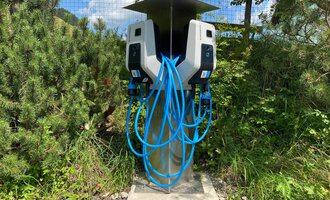 A modern charging station for electric vehicles with multiple charging ports. Surrounded by green vegetation and under a sunny sky. | © Kleinwalsertal Tourismus